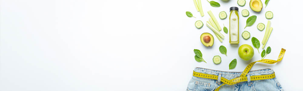 Green veggies and fruit laying out above a pair of jeans with a measuring tape around the waist - symbolizing weight loss Green veggies and fruit laying out above a pair of jeans with a measuring tape around the waist - symbolizing weight loss